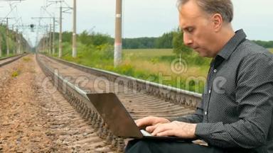 一个男人坐在铁轨上，在笔记本电脑上写着一封信。